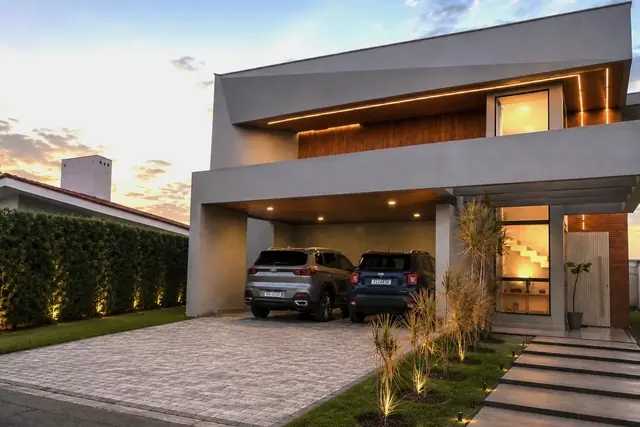 Frente da casa duplex com garagem para dois carros, jardim e caminho de entrada ao fim da tarde